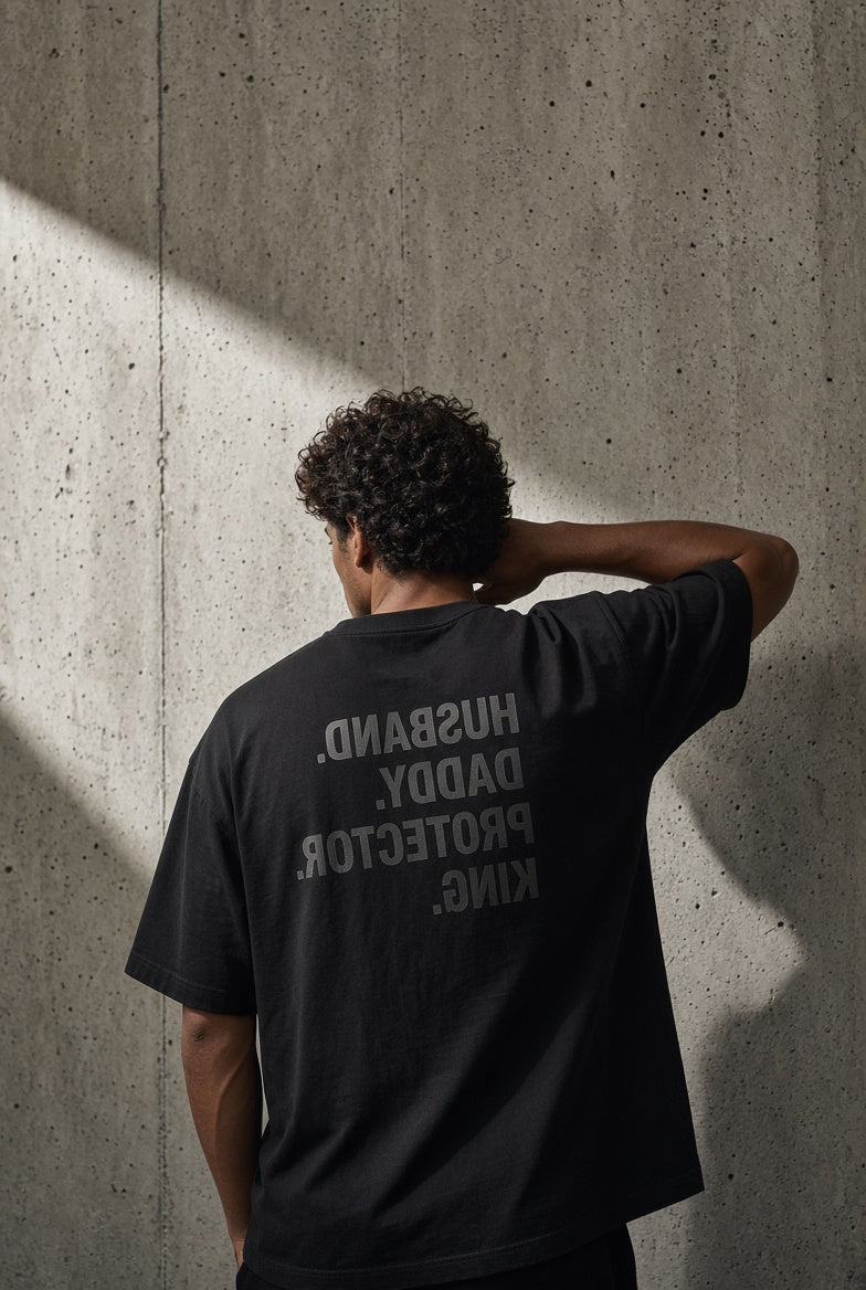 Model wearing the DOMN Husband Daddy Protector King heavyweight T-shirt in Obsidian Black, mirrored back print